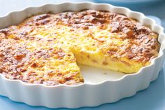 a quiche is shown in a white dish on a blue tablecloth with a slice missing from it