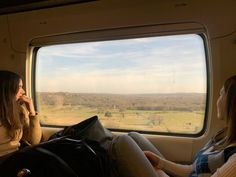 two women looking out an airplane window at the landscape outside their cabin windows, while sitting on a seat