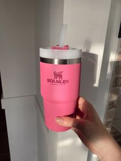 a hand holding a pink tumbler cup in front of a white door with the word stanley on it