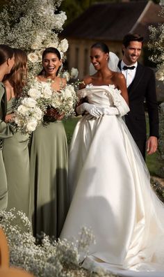 a group of people standing around each other in front of flowers and trees at a wedding