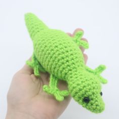 a small green crocheted gecko sitting on top of someone's hand