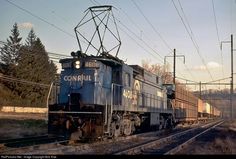 a train is traveling down the tracks near some power lines and telephone poles with trees in the background