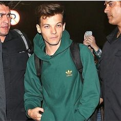 a young man in a green hoodie is holding his cell phone while standing next to two other men