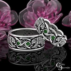 two wedding rings with green stones in the middle and celtic designs on each ring, surrounded by pink flowers