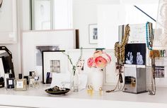 a white counter topped with lots of framed pictures and vases filled with pink flowers