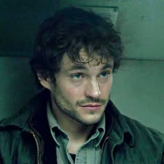 a man with curly hair and blue eyes stares into the camera while wearing a leather jacket