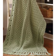 a green crocheted blanket sitting on top of a wooden floor next to a chair