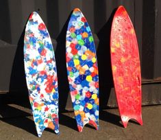 three colorful surfboards are lined up against a black wall with paint splatters all over them