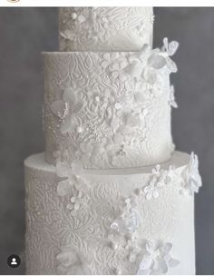 a three tiered white wedding cake with flowers on it's side and the top layer is covered in frosting