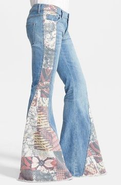 a woman wearing flarey jeans with floral print on the side and bell bottoms, standing in front of a white background