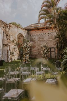 chairs and tables set up in the grass near an old brick building with palm trees