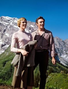 a man standing next to a woman on top of a mountain