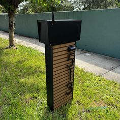 a black and brown mailbox sitting on top of grass next to a tree in front of a fence