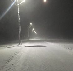 a street light in the middle of a snow covered road at night with no one on it