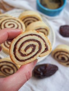 a hand holding a small cinnamon roll in front of some raisins on a plate