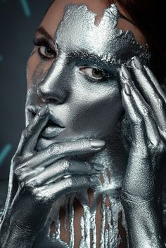 a woman with silver paint on her face and hands near her face, posing for the camera