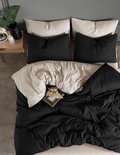 an unmade bed with black and white comforter on it, next to a plant