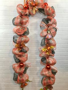 an orange and black wreath with pumpkins hanging from it's sides in front of a brick wall