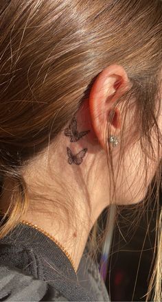 a woman with a small butterfly tattoo on her left side behind the ear is looking down