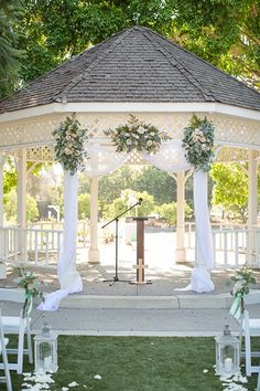 the gazebo is decorated with white flowers and greenery for an outdoor wedding ceremony