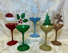 four wine glasses decorated with christmas decorations and glitters on a white tablecloth background