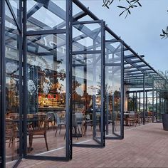 an outdoor dining area with glass walls and wooden tables in the center, surrounded by brick pavers