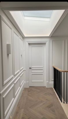 an empty hallway with wooden floors and white walls, leading to a skylight above the door