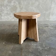 a small wooden stool sitting on top of a cement floor next to a concrete wall