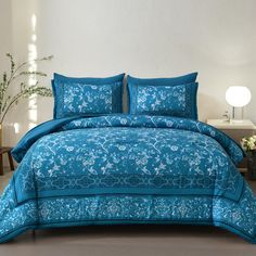 a bed with blue comforters and pillows in a white room next to a plant