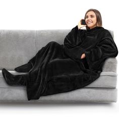 a woman is sitting on a couch and talking on the phone while wrapped in a blanket