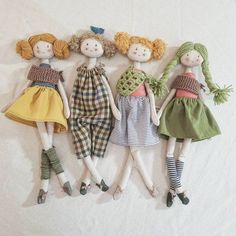 five dolls are lined up in a row on a white surface, one is wearing a green dress and the other has yellow hair