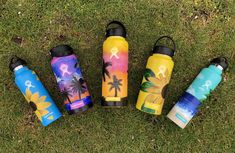 five water bottles sitting in the grass with palm trees and flowers painted on one side