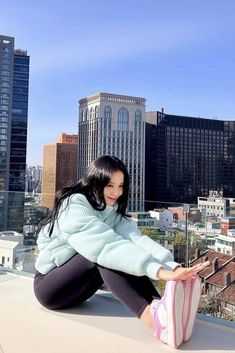 a woman sitting on top of a roof next to tall buildings