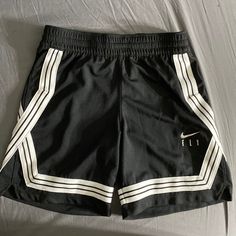 1. Pair Of Shorts 2. Hanging On A Wall 3. Black Color 4. Nike Brand 5. White Stripes On Sides 6. Word "Fly" Written On Right Leg 7. Nike Swoosh Above "Fly" 8. Made For Basketball 9. Athletic Style 10. Elastic Waistband 11. Drawstring For Adjustment 12. Lightweight Material 13. Breathable Fabric 14. Knee-Length 15. Loose Fit 16. Double-Stitched Seams 17. Moisture-Wicking Technology 18. Suitable For Sports 19. Trendy Design 20. Comfortable Wear Cheap Nike Black Athletic Shorts, Nike Fly Basketball Shorts, Affordable Black Nike Athletic Shorts, Basketball Shorts Women Outfit, Womens Basketball Shorts, Western Fits, Nike Basketball Shorts, Athletic Clothes, Basketball Clothes