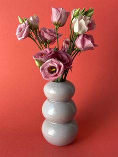 a white vase filled with pink flowers on top of a red table next to a stack of rocks