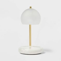 a white table lamp with a gold base and a glass shade on the top, against a white background