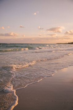 the ocean waves are rolling in and out onto the beach at sunset with clouds overhead