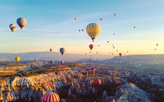 many hot air balloons are flying in the sky over rocks and boulders at sunrise or sunset