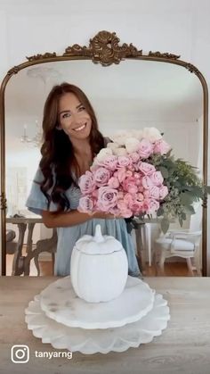 a woman holding a bouquet of flowers in front of a mirror with a teapot on it