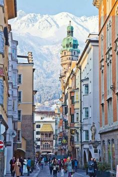 people are walking down the street in front of buildings with mountains in the back ground