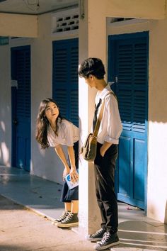 two people standing next to each other on the sidewalk in front of blue shuttered doors