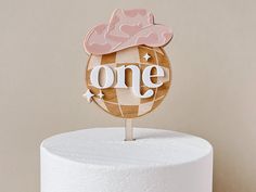 a cake topper with the word one on it and a pink hat on top