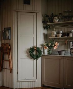 a white door in a kitchen next to a shelf with flowers and plates on it