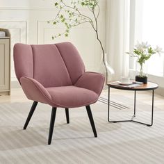 a pink chair sitting on top of a rug next to a vase with flowers in it