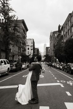 a bride and groom kissing in the middle of an empty street with cars parked on both sides