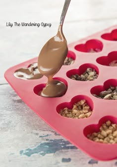 a spoon is pouring chocolate into a heart shaped muffin pan