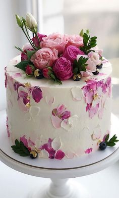 a white cake with pink and purple flowers on it sitting on a table next to a window