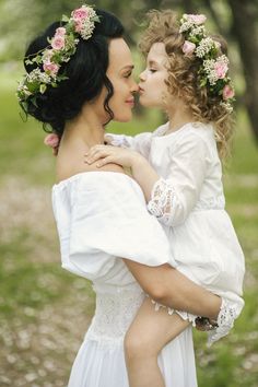 two women in white dresses with flowers on their heads and one holding the other woman's head