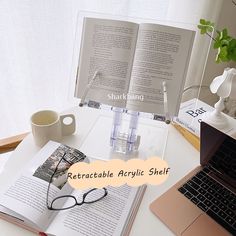 an open book sitting on top of a desk next to a laptop computer and coffee cup