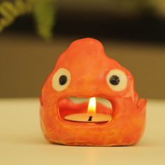 an orange candle holder with a lit candle in the shape of a monster's mouth